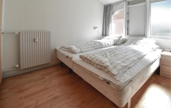 Un dormitorio con una cama individual, un radiador, una ventana con cortinas y suelo de madera.