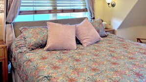 A bedroom with a floral bedspread, a wooden headboard, and a window with blinds.