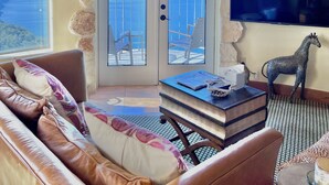 A living room with a leather sofa, a small table with books, a giraffe statue, and a TV mounted on the wall.