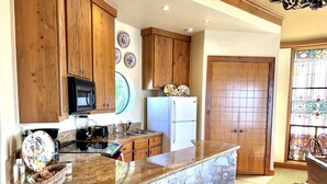 A kitchen with wooden cabinets, a granite countertop, a microwave, a toaster, and a refrigerator. - Top apartment #3 of the Castle ~ Sunsets & views high above Lake Travis! (Austin)