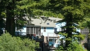 A two-story house with a balcony, surrounded by dense greenery. - Grandma's House: Riverfront, Gorgeous View, Beach/Swimming/Canoeing Dog Friendly (Monte Rio)