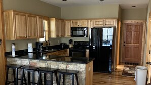 A spacious kitchen with wooden cabinets, a central island with stools, a microwave, a refrigerator, and a stone backsplash.