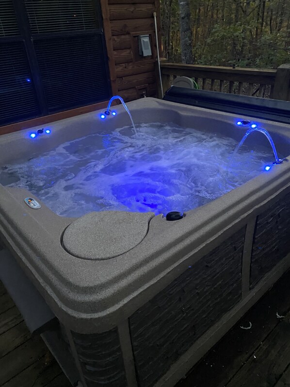 A hot tub with blue LED lights, a control panel, and a wooden deck surrounding it.