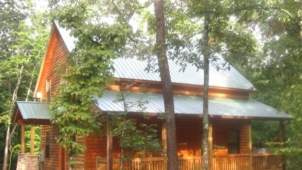 A wooden cabin with a porch, surrounded by trees.