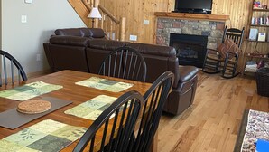 A dining area with a wooden table and chairs, a sofa, and a fireplace.