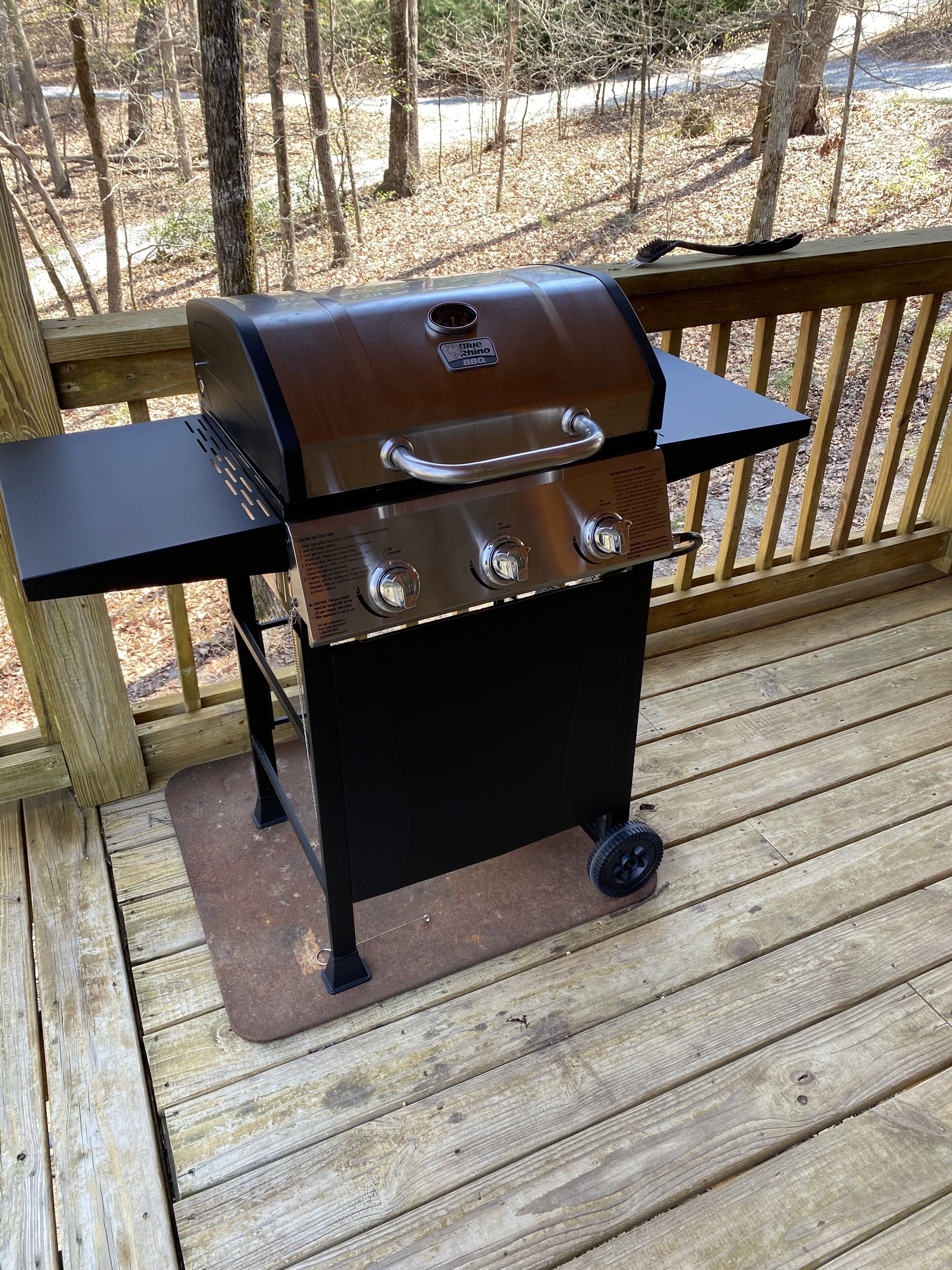 Un barbecue portable sur une terrasse en bois, avec une rambarde en métal.