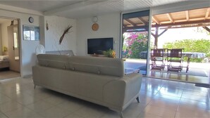 Een woonkamer met een bank, een flatscreen-tv, decoratieve muurkunst en een glazen schuifdeur die leidt naar een terras.