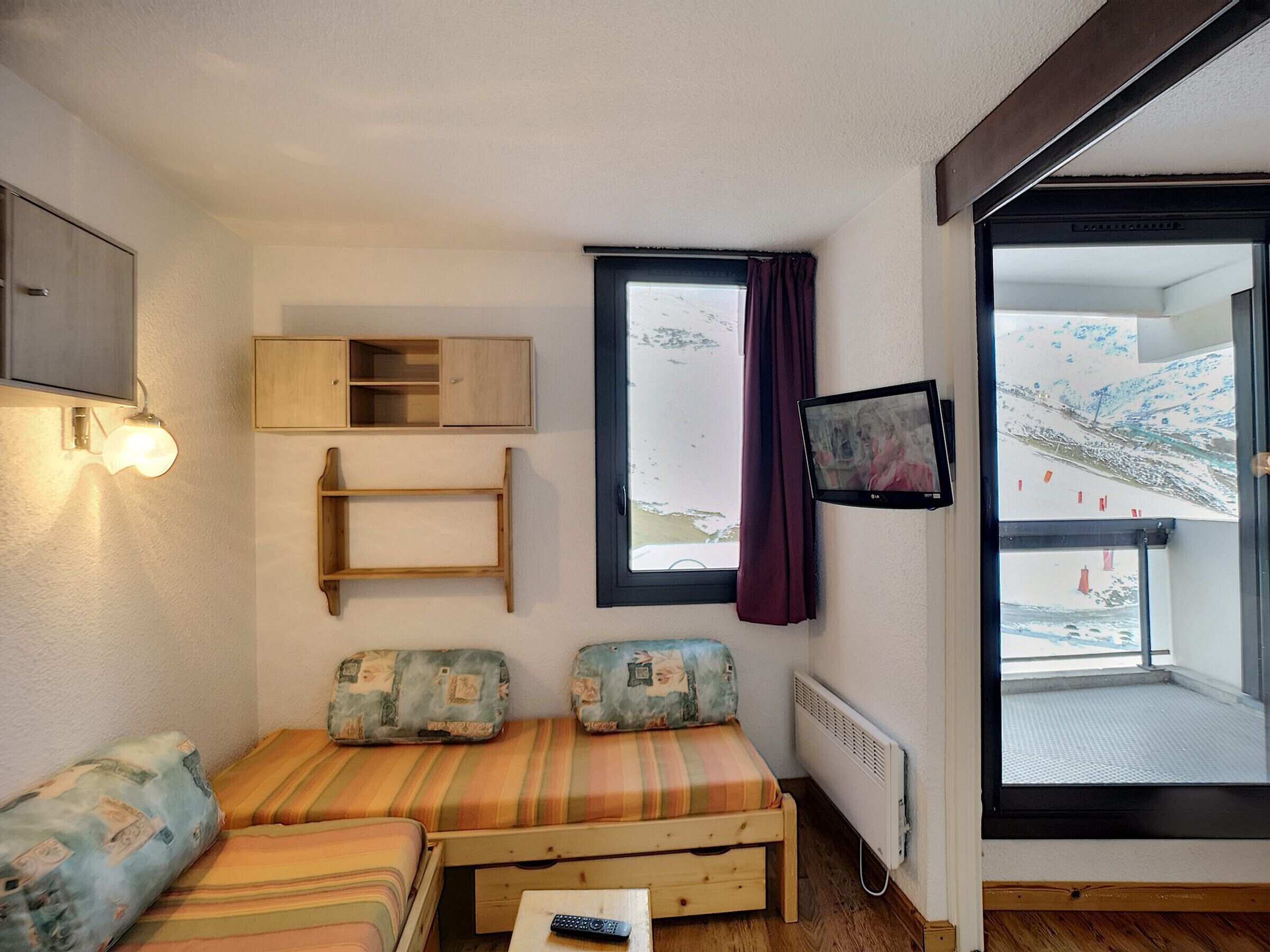 Een knus kamertje met een bed, een televisie en een raam met uitzicht op een besneeerd landschap.