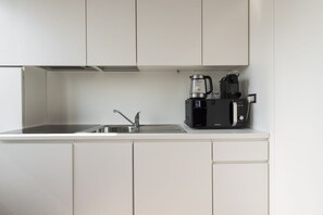 Una cocina con un lavamanos de acero inoxidable, una cafetera y un microondas.