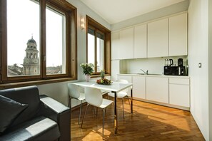 A modern kitchen with white cabinets, a dining table with chairs, a coffee machine, and a view of a historic building through large windows. - Panoramic apartment equipped with every comfort 2 minutes from the Duomo (Milano)