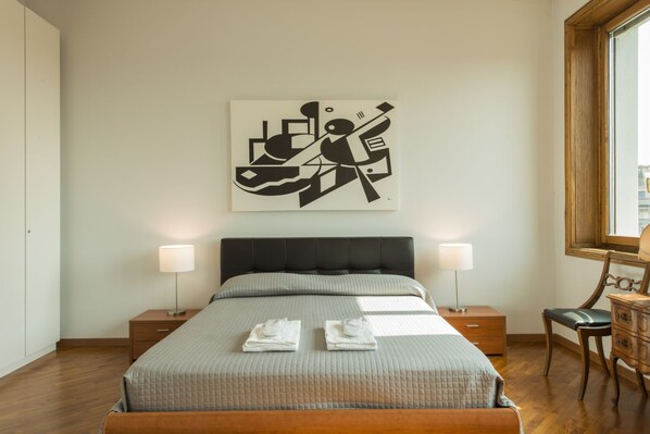 Une chambre à coucher avec un lit, deux tables de chevet, une commode, une chaise et un tableau accroché au mur.