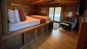 Ein Holzblockhaus-Interieur mit einem Bett, einem Sessel und einem Kamin.