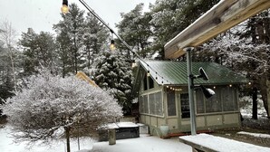 Eine kleine Holzhütte mit einem grünen Dach, umgeben von schneebedeckten Bäumen und einem Holzzaun.