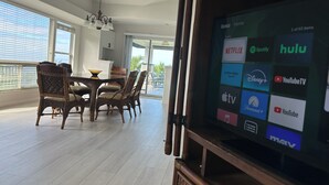 Un'ampia zona giorno con tavolo da pranzo, ampie finestre e televisore che mostra diversi servizi di streaming.