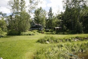 Relax by the serene water's edge, surrounded by lush greenery and a simple, functional building in the background.