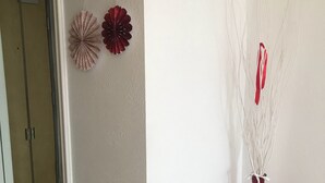 Un corridoio con una porta, uno specchio a parete e un vaso rosso con rami bianchi.