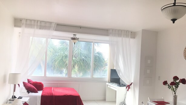 Una camera d'albergo con un letto, una scrivania con un computer, un tavolo da pranzo con sedie e una finestra con tende.