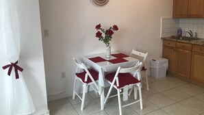 Una piccola cucina pulita con mobili bianchi, una parete rivestita di piastrelle e un tavolo da pranzo apparecchiato con tovaglioli rossi e sedie bianche.