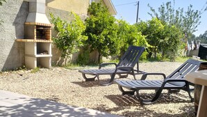 Un espace patio comprenant deux chaises longues, un mur en pierre et un petit four d’extérieur.