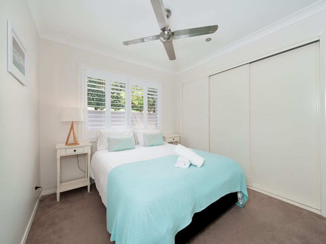 A bedroom with a bed, a nightstand, a ceiling fan, and a window with blinds.