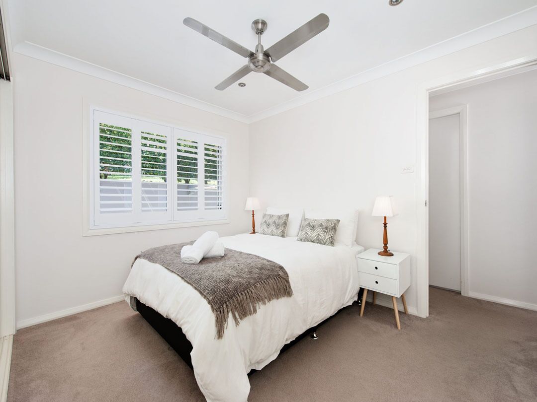 A bedroom with a bed, bedside tables, a ceiling fan, and a window with blinds.