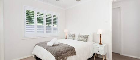 A bedroom with a bed, bedside tables, a ceiling fan, and a window with blinds.