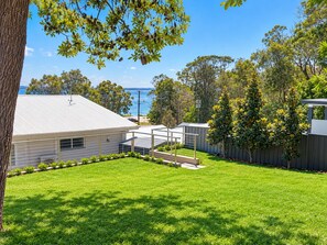 A residential property with a well-maintained lawn, a house with a metal roof, and a view of the sea. - Beachside Haven - Your Perfect Oasis Home (Corlette)