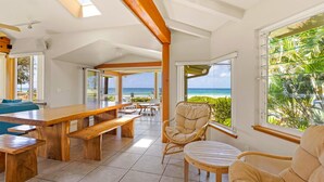 Un espacio interior amplio con una mesa y sillas de madera, ventanas grandes con vista al océano y un techo alto con vigas a la vista.