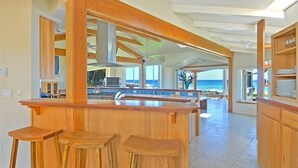 Una cocina amplia con una isla grande, taburetes de madera y vista al océano.
