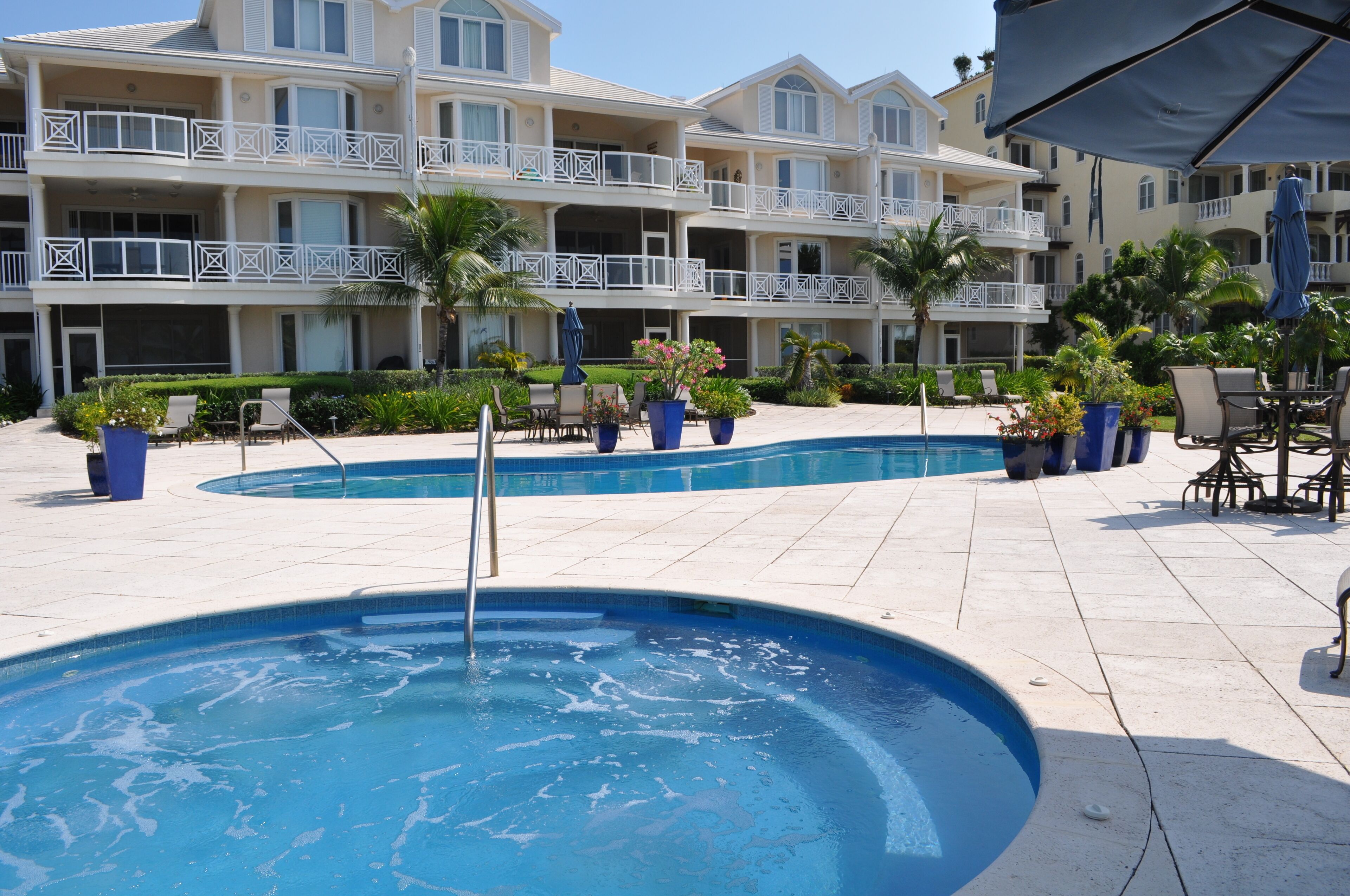 Un área de piscina con varias piscinas, sillas de descanso y sombrillas.