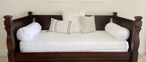 A dark wood four-poster bed with a white quilt and pillows, two framed pictures on the wall above, and a tiled floor.