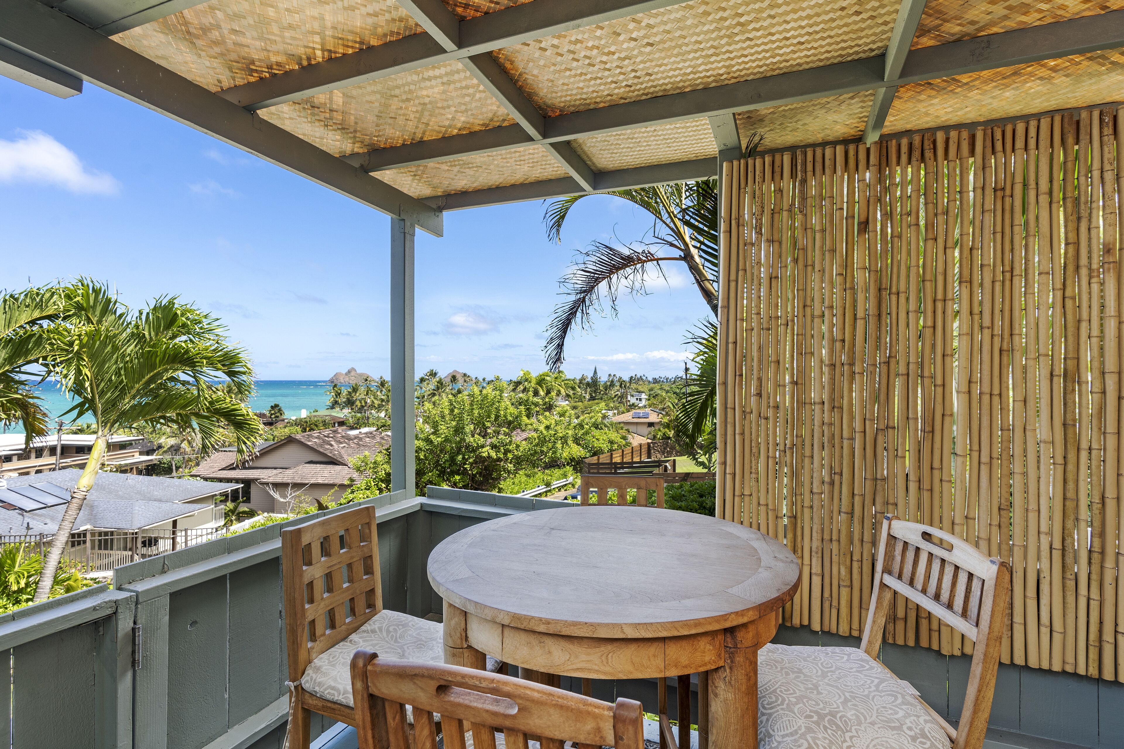 Un balcon avec une table ronde et des chaises, donnant sur une plage et une végétation luxuriante.