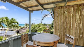 Un balcon avec une table ronde et des chaises, donnant sur une plage et une végétation luxuriante.