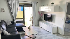 Ein modernes Wohnzimmer mit einer schwarzen Ledersofa, einem Holztisch, einem Flachbildfernseher und einer Glastür zum Balkon.