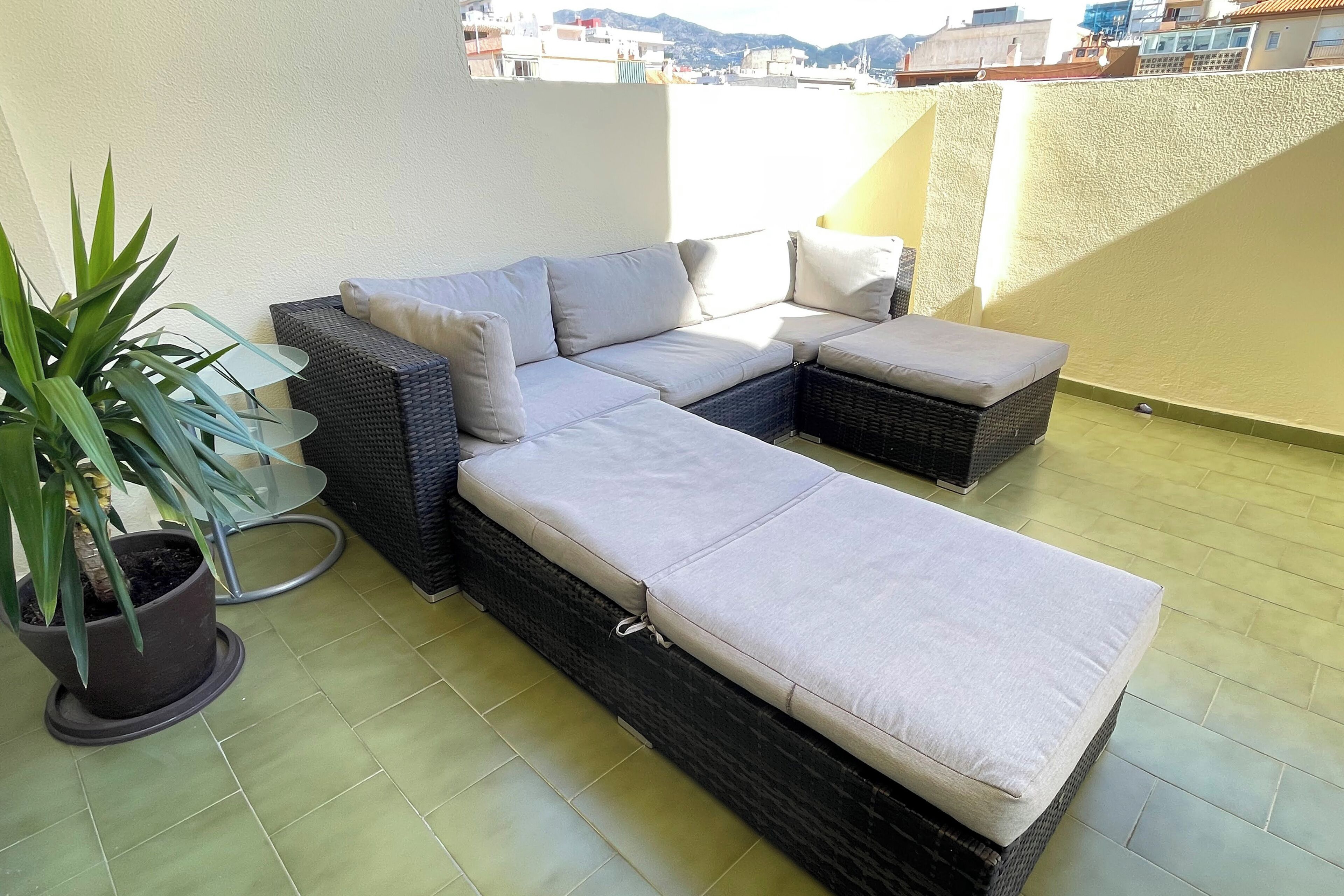 Un balcón con sofá, reposapiés, una planta en maceta y vistas a edificios.