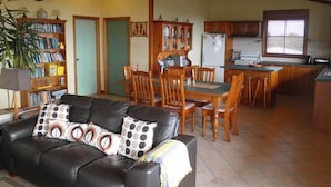 Ein Wohnzimmer mit einer Ledersofa, einem Holzesstisch und Stühlen, eine Küche mit Holzschränken und ein großes Fenster.