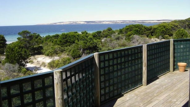 Eine Holzterrasse mit Blick auf das Meer und viel Grün.