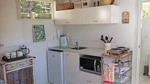 A compact kitchen with white cabinets, a small refrigerator, a microwave, and a coffee maker.