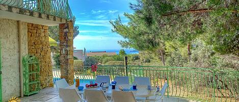 Eine Terrasse mit Tisch und Stühlen mit Blick auf eine malerische Landschaft aus Meer und Bäumen.
