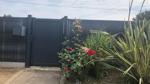 En sort metalport med et lille haveområde ved siden af, inklusive røde blomster og grønne planter.