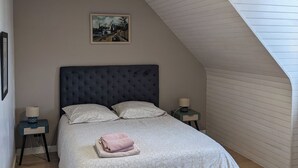 Et soveværelse med skrå væg, en stor seng, et sengebord, en stol og et billede på væggen.