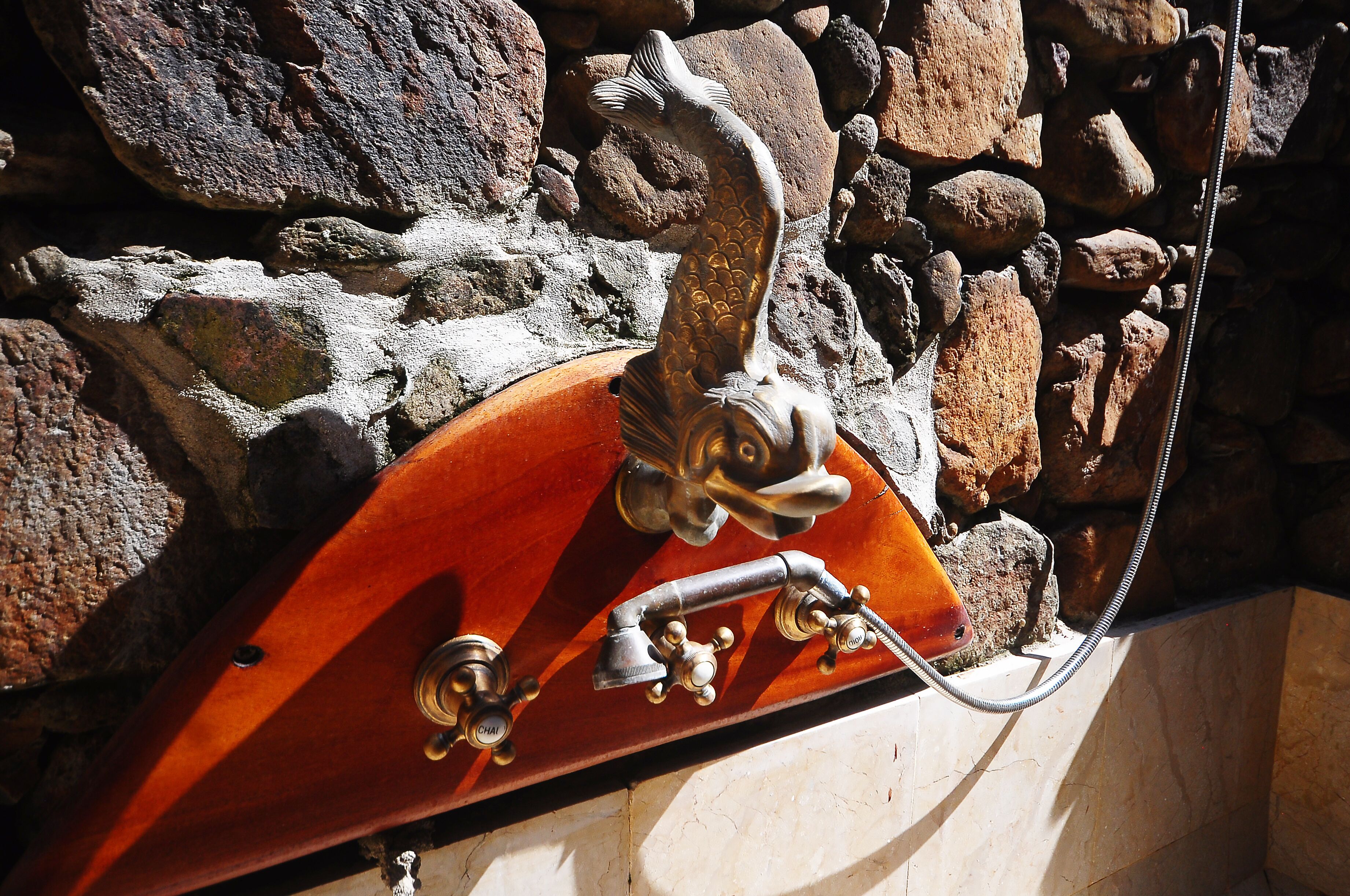 Eine hölzerne Badewanne mit Fischmotiv, vor einer Steinwand platziert.