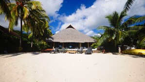A beachside resort with a thatched-roof building, lounge chairs, and palm trees.