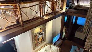 A high-ceilinged room with a thatched roof, a sofa, a television, and a painting on the wall.