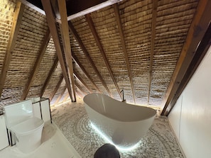 Un baño en el desván con bañera, vigas de madera y techo de paja.