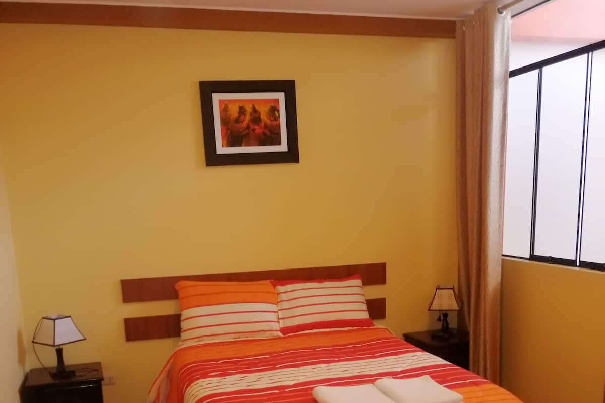 Uma cama bem arrumada com roupa de cama listrada, um quadro na parede e uma janela com cortinas.