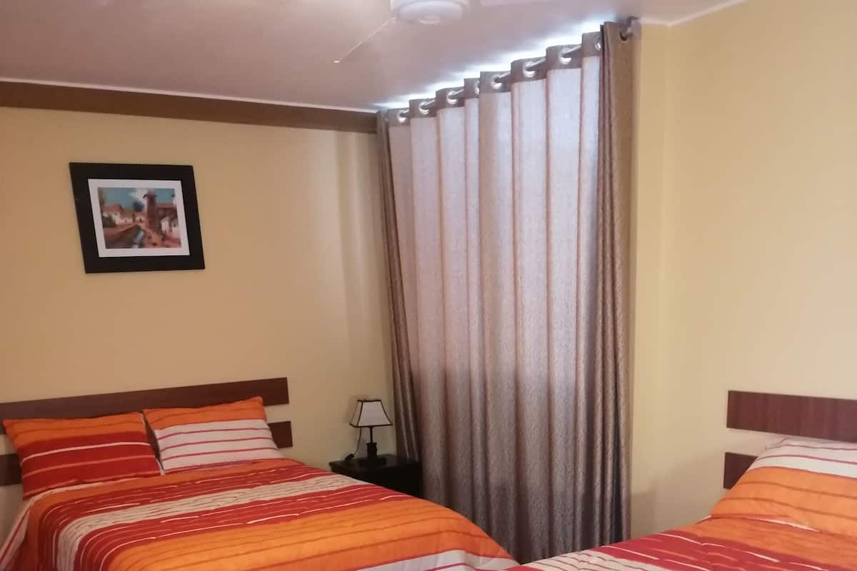 Quarto de hotel com duas camas, cabeceiras de madeira e roupa de cama listrada.