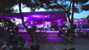 An outdoor seating area with tables and chairs, surrounded by trees. - Luxury 5* apartment overlooking 2 swimming pools.  (Peyia)