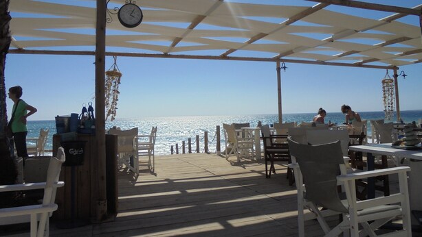 A wooden deck with outdoor seating, a clock, and a view of the sea. - Luxury 5* apartment overlooking 2 swimming pools.  (Peyia)