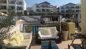 A balcony with outdoor furniture, a pool, and a view of surrounding buildings. - Luxury 5* apartment overlooking 2 swimming pools.  (Peyia)